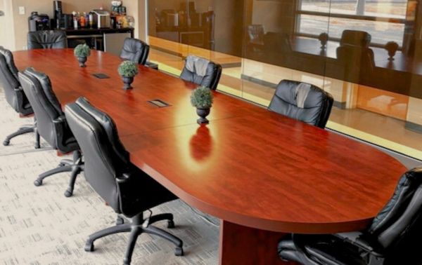 A modern conference room at the GWC Community Center, featuring a long wooden table with eight black leather chairs, a coffee station in the corner, and large glass windows reflecting the room’s natural light.